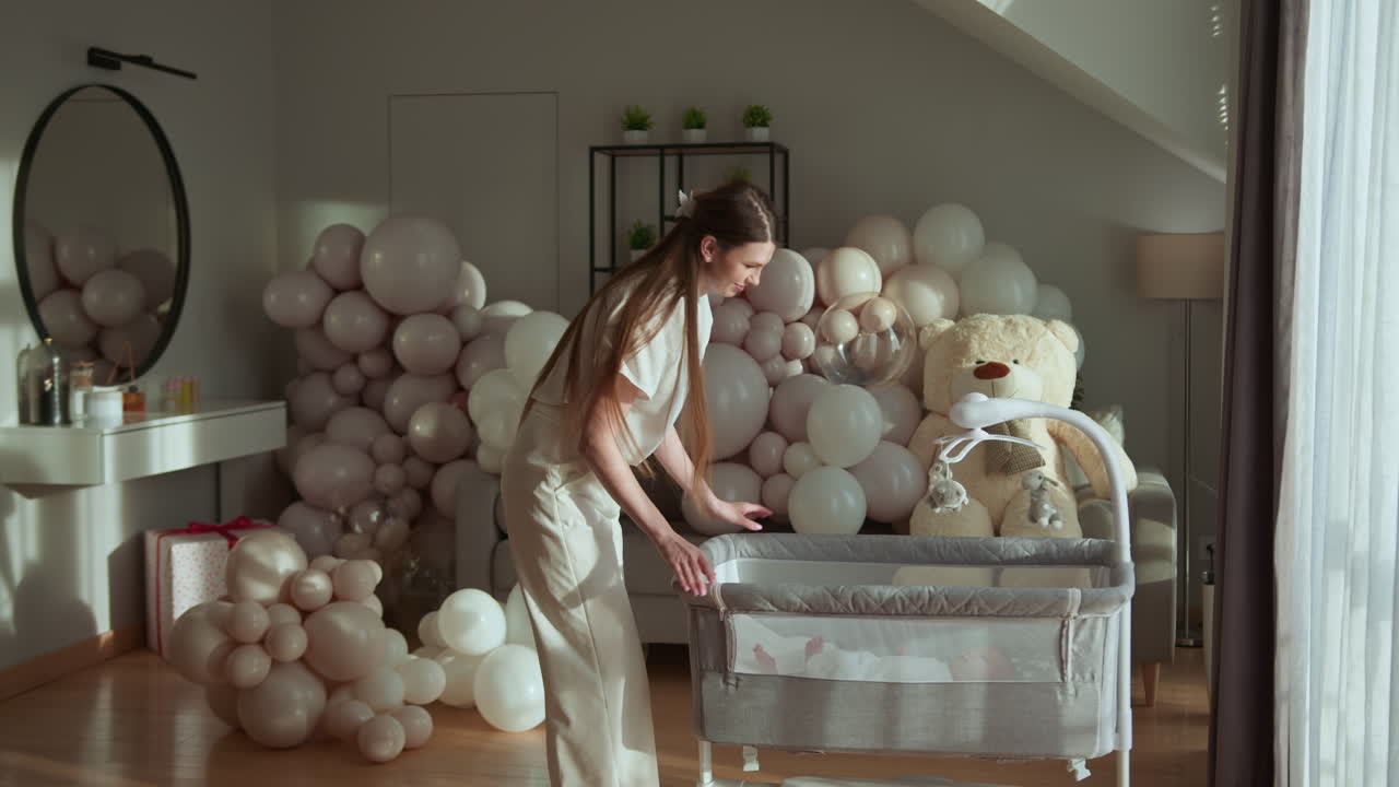Donna che prepara la culla per il bambino, circondata da palloncini festivi e un orsetto di peluche, creando una cameretta gioiosa.