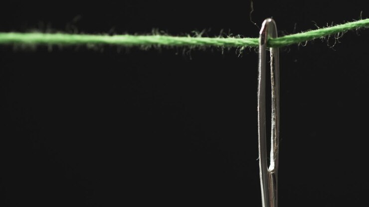 Video of micro of green thread going through needle with copy space on black background