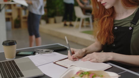 joven mujer de negocios caucásica escribiendo notas disfrutando del estudio escuchando música usando auriculares estudiante trabajando en una oficina multiétnica ocupada