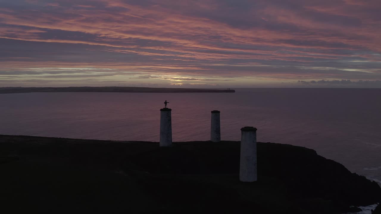 Purple dawn sunrise aerial of Metal Man beacon on Irish coast cliff