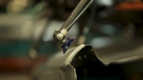 Close-up-of-a-silver-robotic-arm-featuring-a-blue-suction-cup-and-white-joint,-positioned-over-an-unidentifiable-black-object-in-an-assumed-factory-backdrop