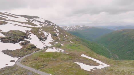 Aerial---vehicles-on-scenic-mountain-pass-in-alpine-landscape,-snow-patches