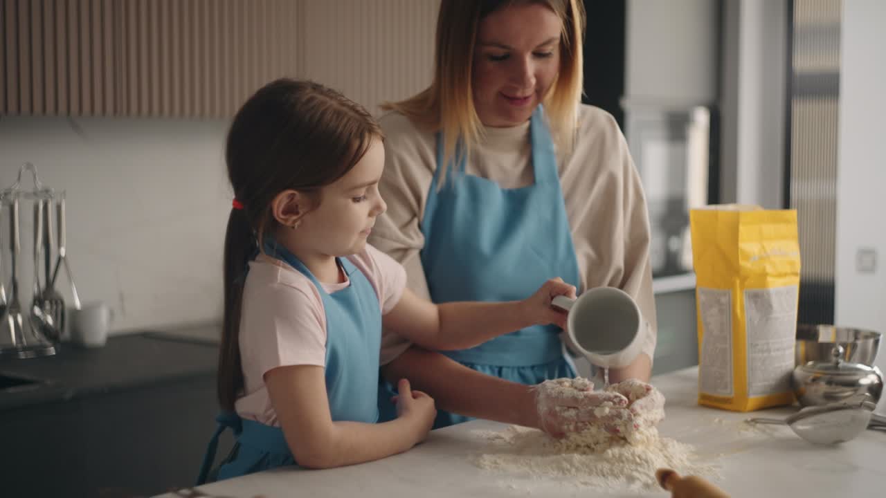 little girl is helping to her mother to make dough for pie, pouring water on flour, woman is kneading by hands