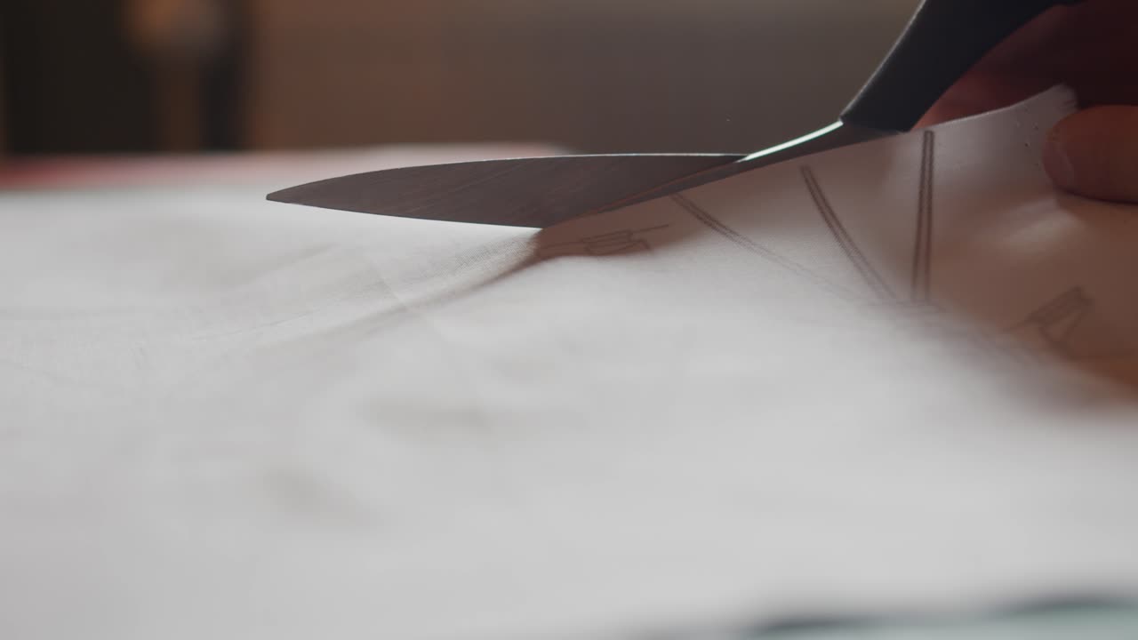 Close up of scissors cutting through pale fabric with natural backlighting