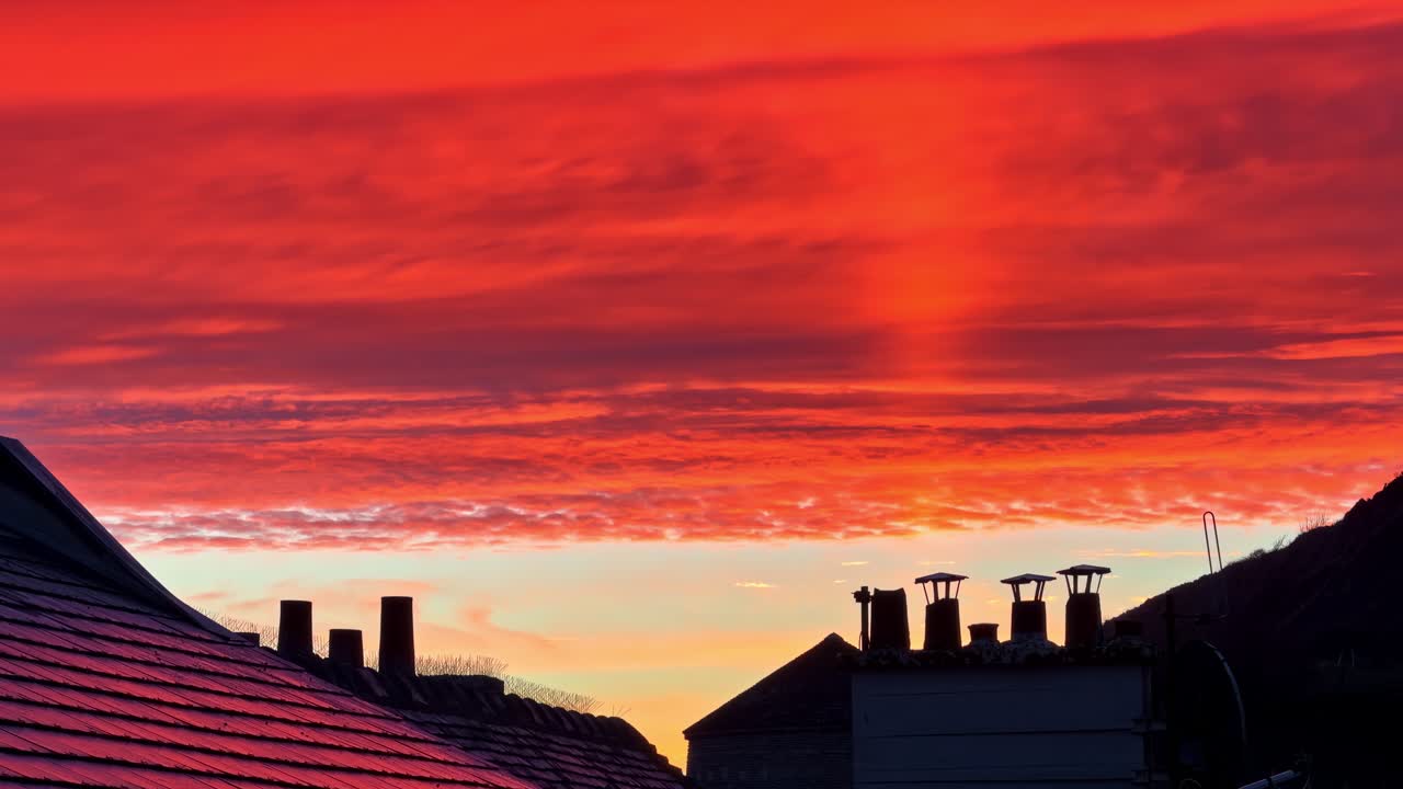 Dark silhouette of traditional French coastal roofs and chimneys against fiery orange sunset sky with bird flying through frame in Port-en-Bessin Normandy