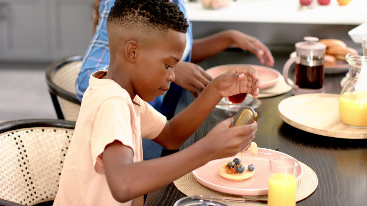 Ragazzo che versa il miele sul pancake durante il pranzo in famiglia al tavolo da pranzo di casa.