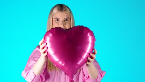 mujer rubia sosteniendo un globo púrpura en forma de corazón, estado de ánimo del día de san valentín con fondo de color azul, toma de estudio