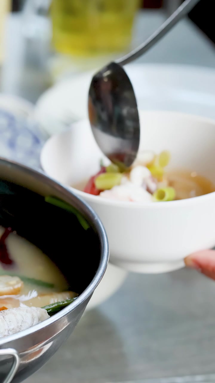 Close-up of a ladle pouring hot seafood soup into a bowl at a restaurant.