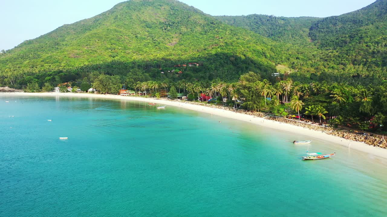 Paradise turquoise bay with calm clear water washing white sandy beach of tropical island with palm trees and green hills, Thailand