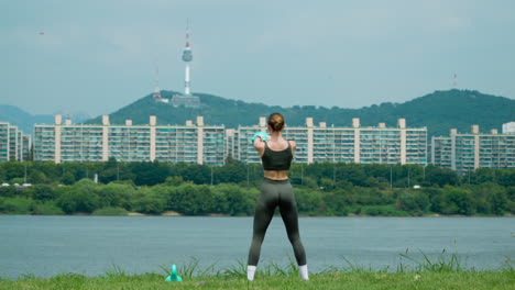 back view of athletic young woman performing american kettlebell swings at han river park with view of n seoul tower in mountain lanscape