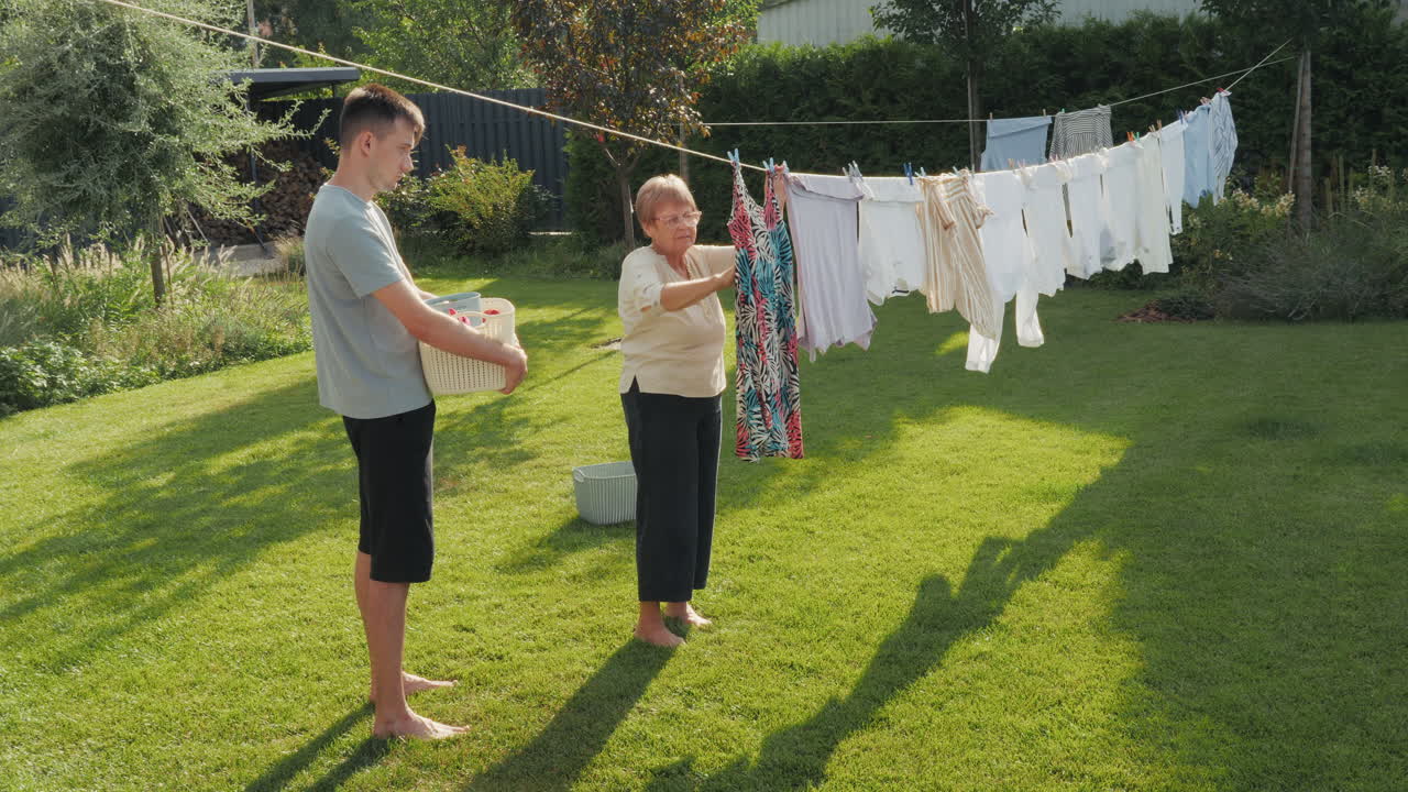 손자가 정원에서 세탁을 하는 할머니를 돕고 있다