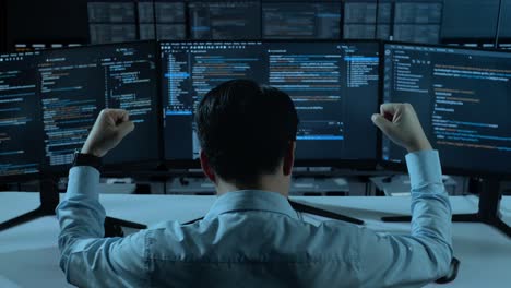 back view of happy asian man developer celebrating while write code with multiple computer screens in the office