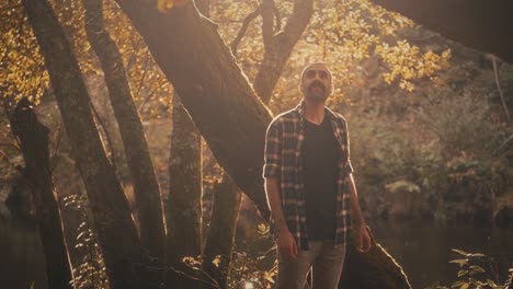 young man walks among trees by river in portugal, backlit by sun. he contemplates golden scenery and feels hopeful. warm and relaxing footage