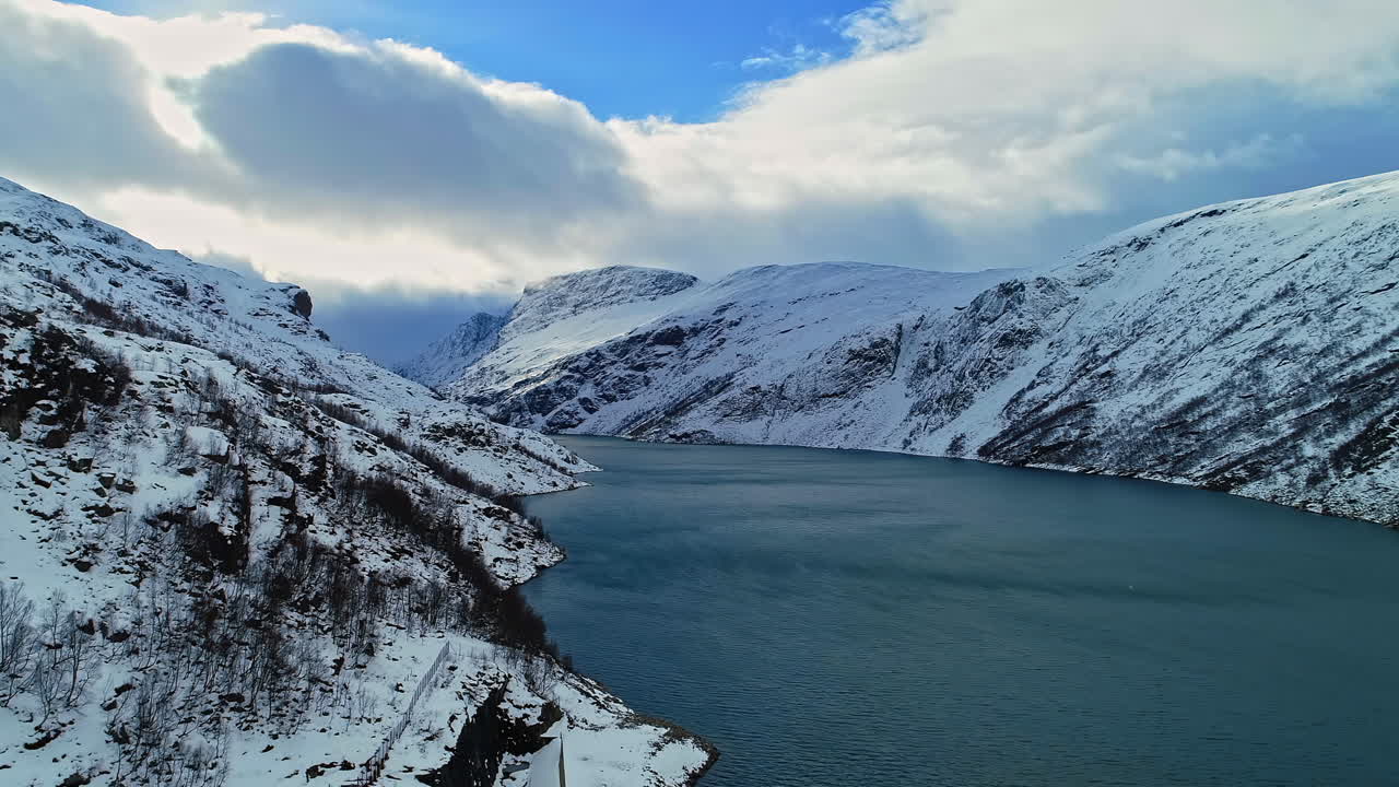 vuelo aéreo que muestra montañas nevadas entre fiordos durante un día soleado en noruega