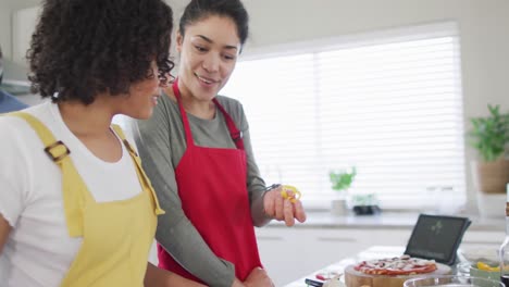sonriendo diversas amigas y amigos con computadora portátil haciendo pizza en la cocina, en cámara lenta
