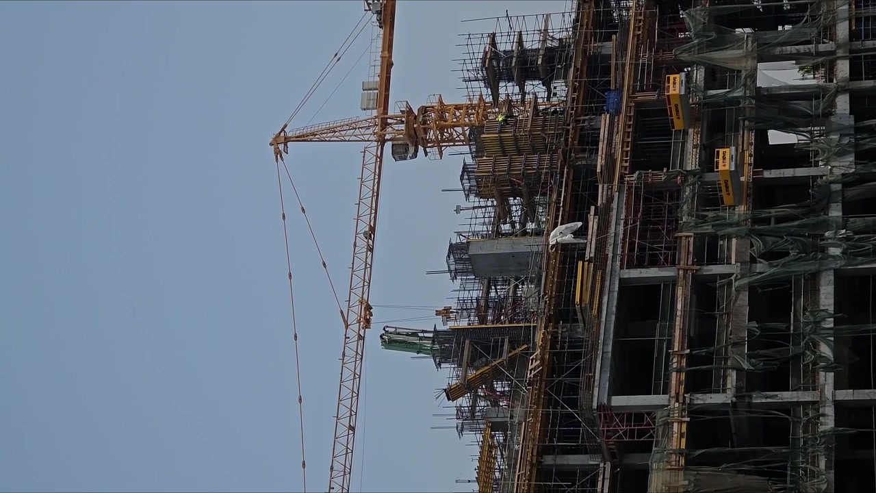 Vertical video building under construction yellow cranes steel structure camera panning right left motion clear sky daytime industrial site urban development architecture progress