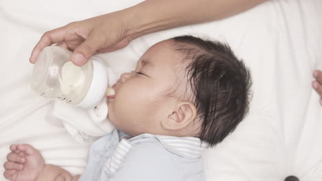 baby boy drinking milk from feeding bottle held by his mother in the bed