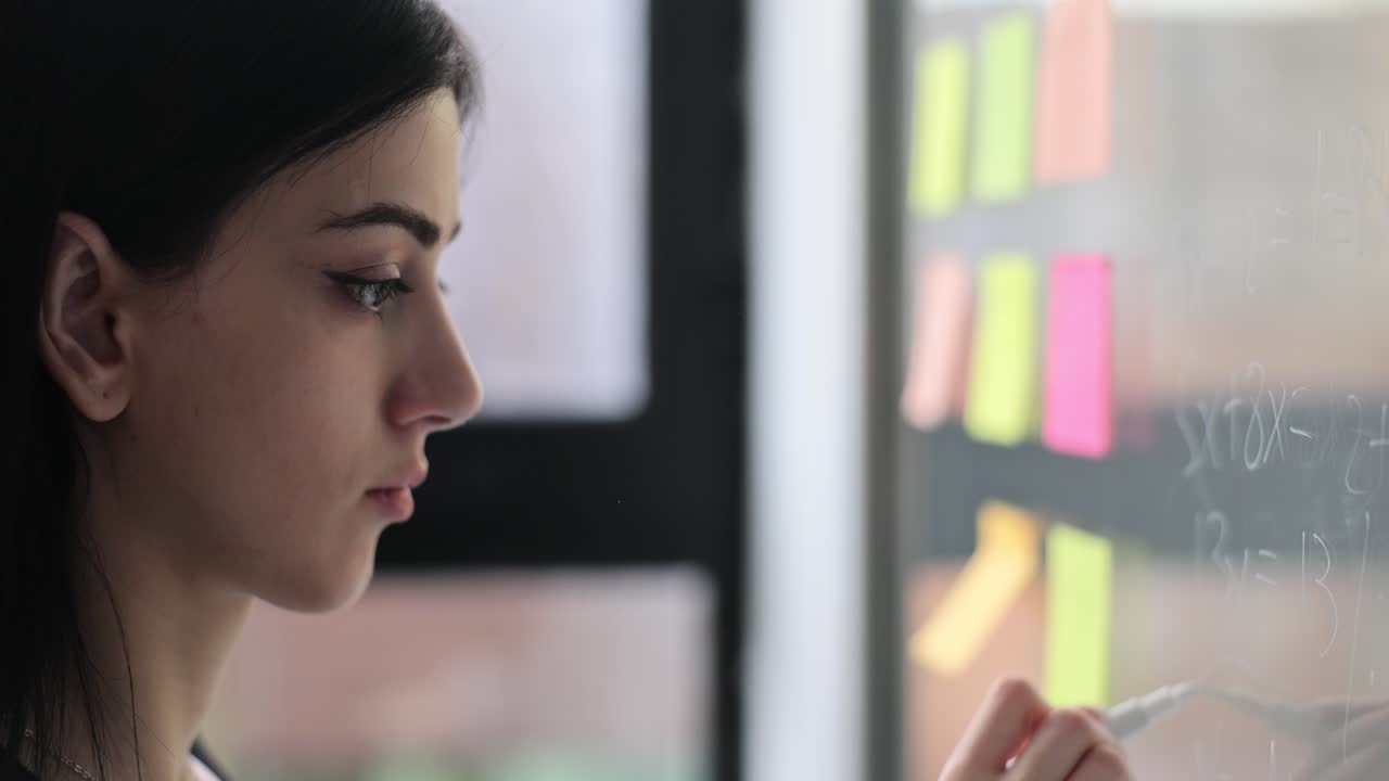 Young woman writing on a glass board with colorful sticky notes