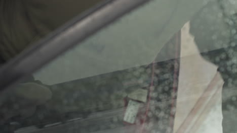 close up of young adult wearing winter jacket gripping chrome handle of red car door to enter vehicle during snowfall, with snow on ground and water droplets visible on car surface and window