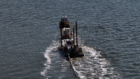 an aerial view of tugboats, and a small barge dredging a bay on long island, new york on a sunny day