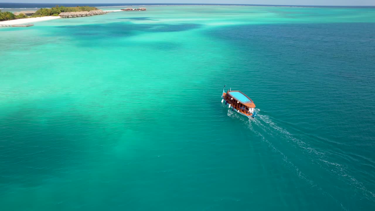 vista aérea de la película del barco dhoni de maldivas a través de la bahía a la isla con bungalows sobre el agua