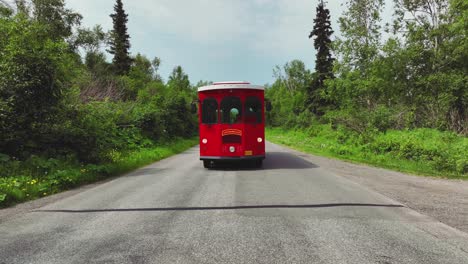 red trolley bus driving slowly on the road in rural alaska - wide shot