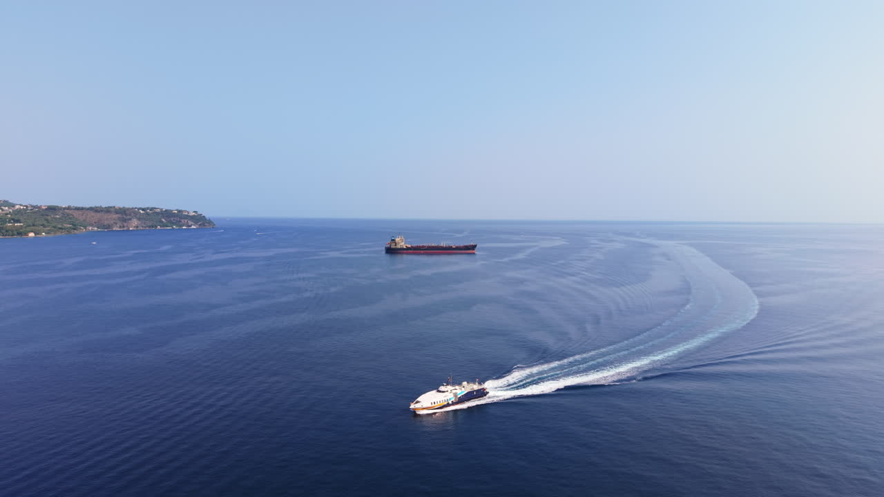 Drone advancing toward an oil tanker while a cruise boat circles and exits the frame, leaving water trails off the Sicilian coast