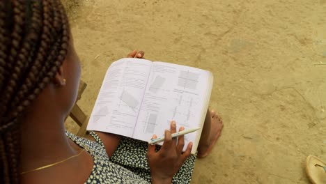 skimming through a mathematics book, a young ghanaian woman is trying to learn the basic of arithmetic in her local village in kumasi, ghana, africa