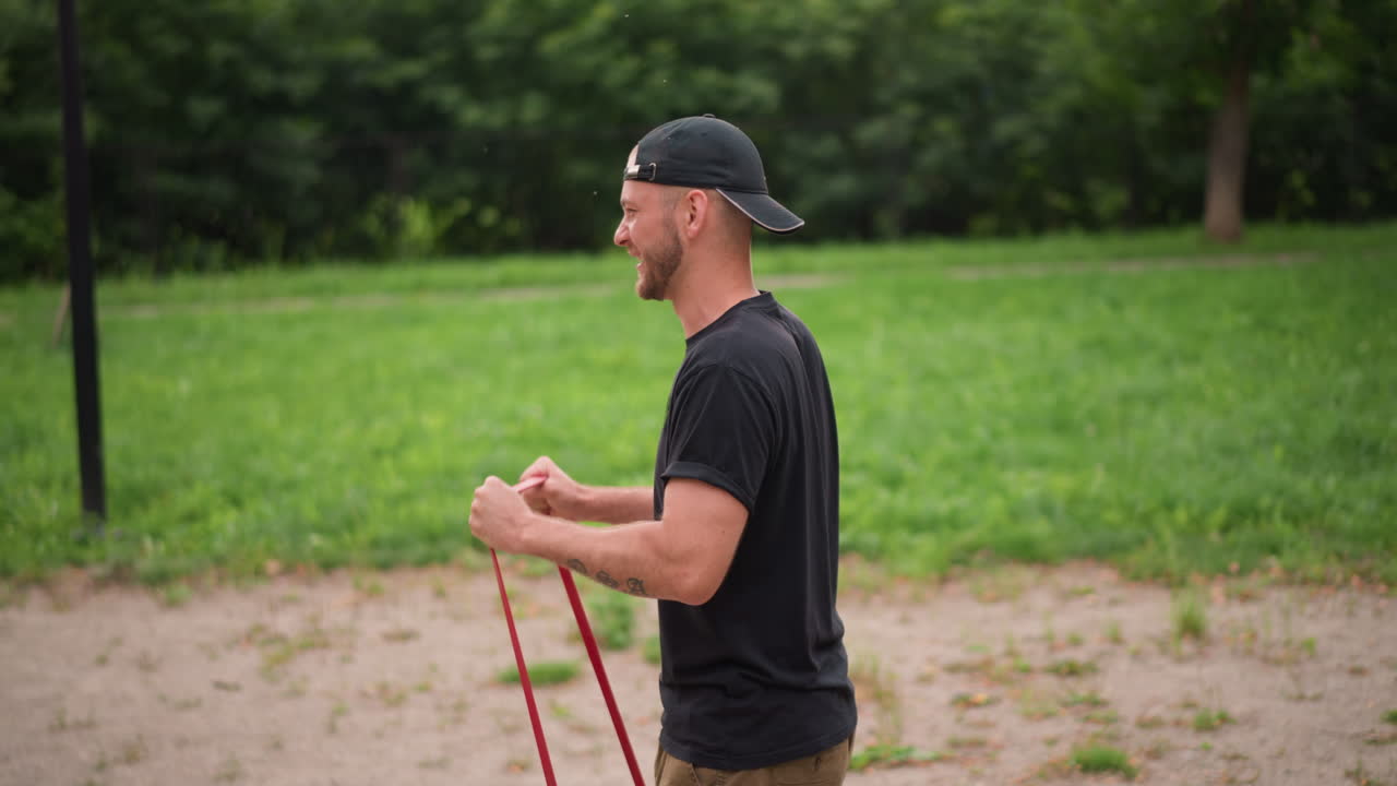 Joyful Outdoor Exercise, Man Enjoys Vigorous Workout In Park With Cheerful Attitude, Casual Man Happily Stretching With Resistance Bands Amidst Green Park Scenery And Lighthearted Laughter