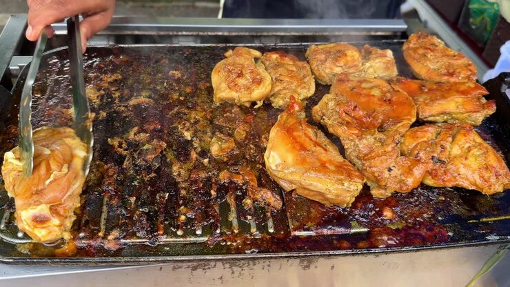Carne di pollo grigliata che viene girata su una griglia aperta.