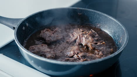 close up of a steaming and boiling beef meat sauce cooking in a pan on the stove in slow motion during a day