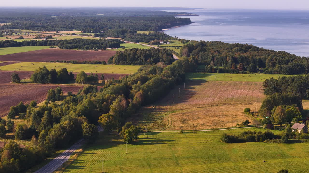 Scenic view of rural Jurkalne fields, tree-lined roads, and distant Baltic shoreline.