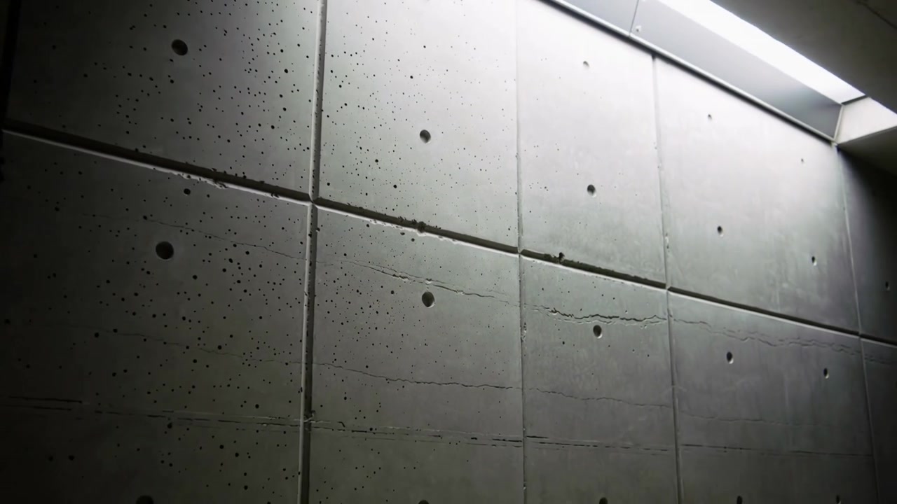 Câmera recuando, revelando painéis pré-moldados em corredor, com fenda de luz projetando-se sobre furos de amarração e rachadura.