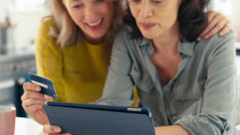 pareja de mujeres maduras del mismo sexo con tarjeta de crédito usando una tableta digital en casa para reservar vacaciones o comprar