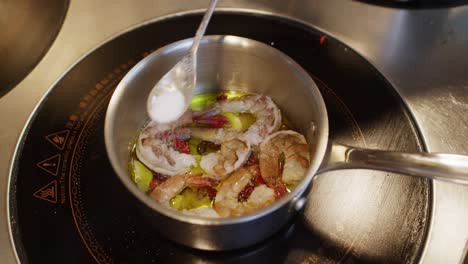 chef add salt while cooking seafood for mediterranean soup in pot over the fire inside a professional restaurant kitchen