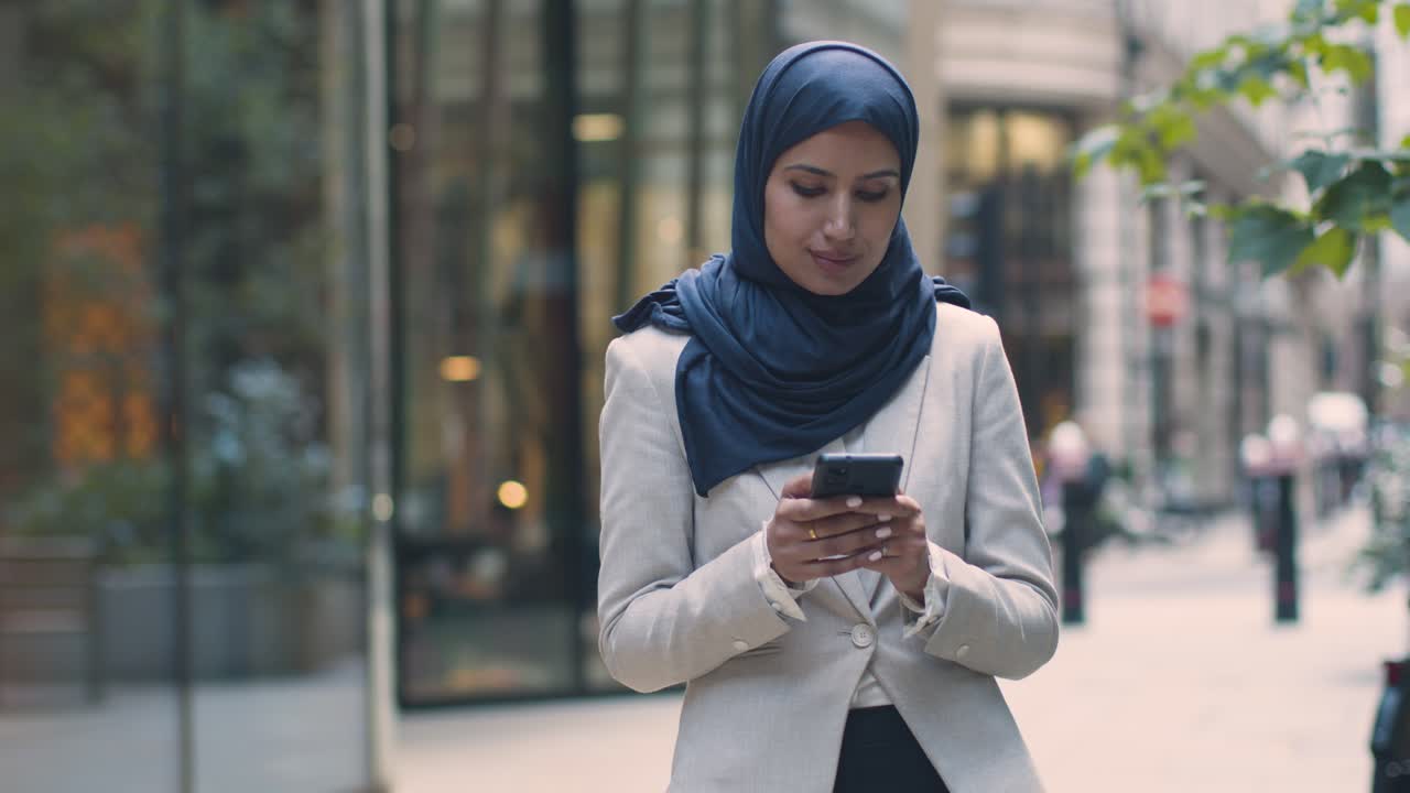 Muslim Businesswoman Checking Messages On Mobile Phone Standing Outside Office In City 2