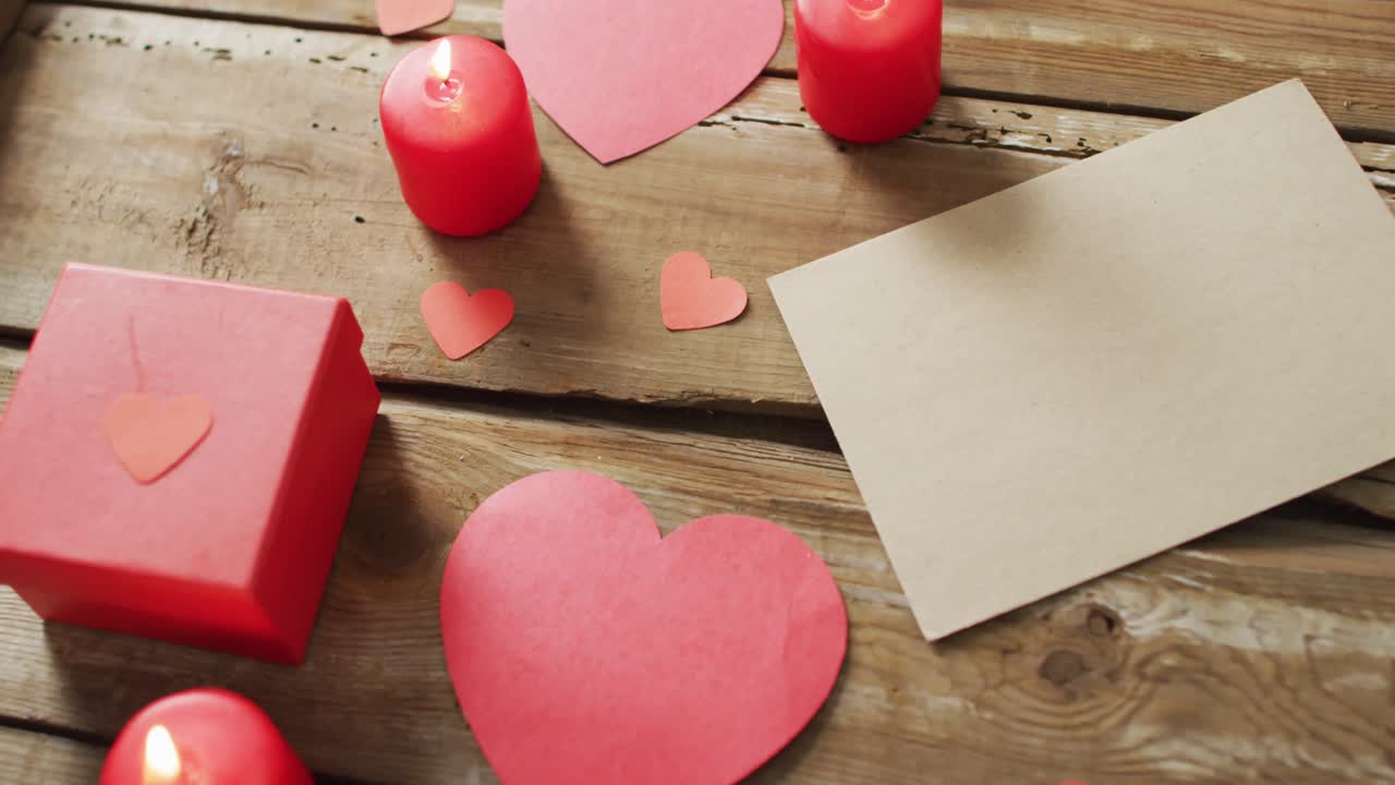 Paper hearts and gift with candles on wooden background at valentine's day