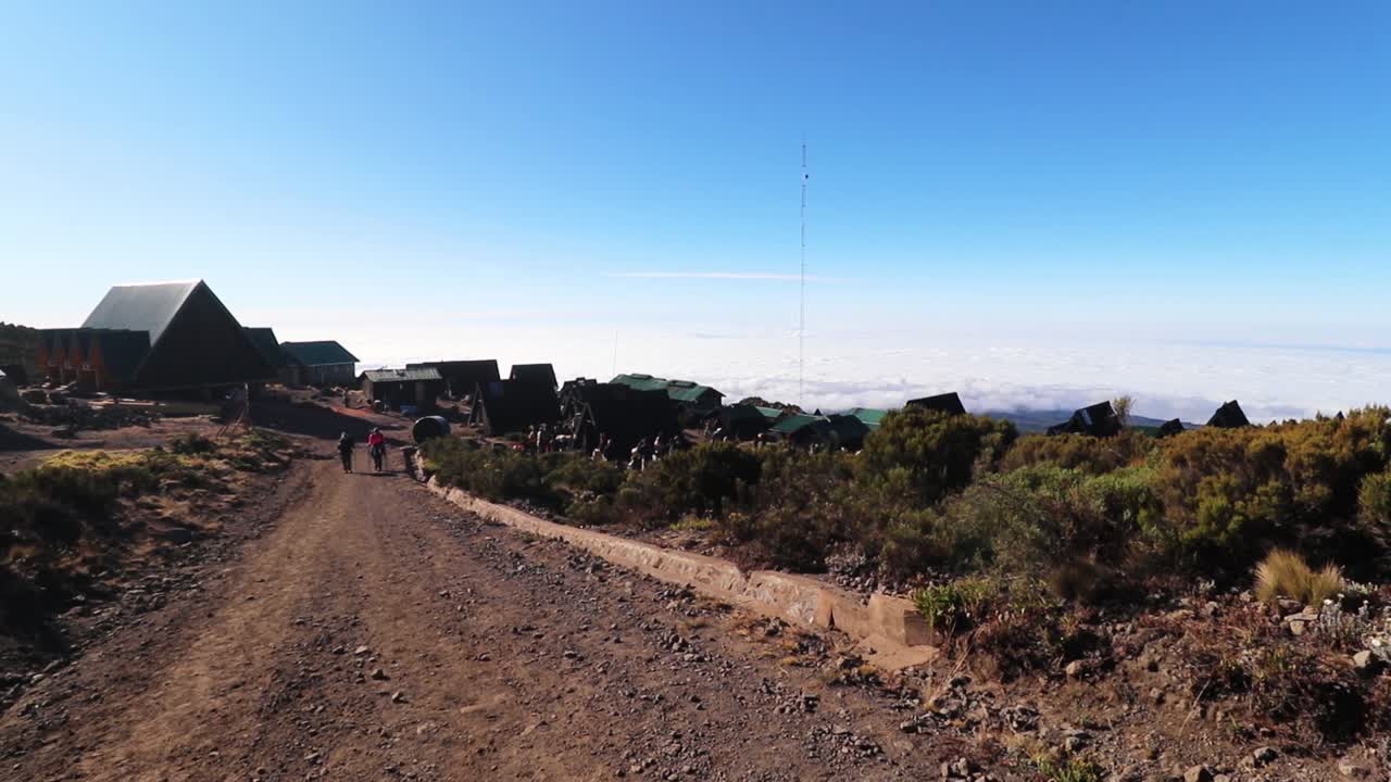 toma estática de un grupo de personas caminando hacia un pequeño pueblo, en el monte kilimanjaro, en un día soleado, en la cabaña horombo, en tanzania, áfrica.