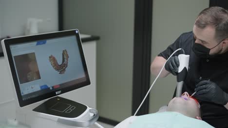 doctor scans the patient's teeth in the clinic. the dentist holds in his hand a manual 3d scanner for the jaw and mouth. dental health. creates a 3d model of teeth and gums on a medical monitor.