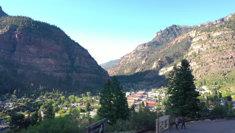 aerial drone rising on lookout point of ouray colorado city downtown, cars and houses surrounded by rocky mountain cliffs and pine tree forest