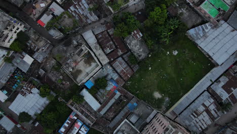 top down aerial slum area with city buildings and little green space - drone ascending shot