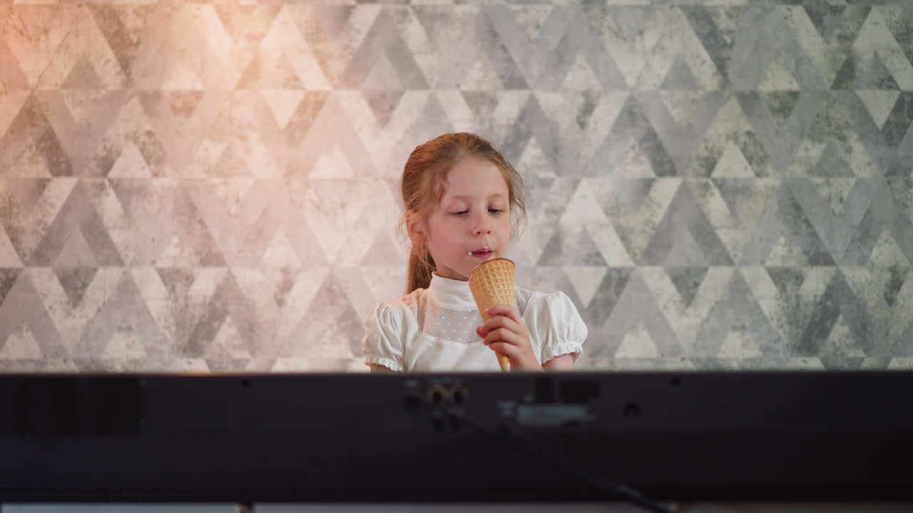 Elegant young girl in white top sitting in front of keyboard piano enjoying ice cream cone with soft glowing light illuminating stylish geometric patterned wall background