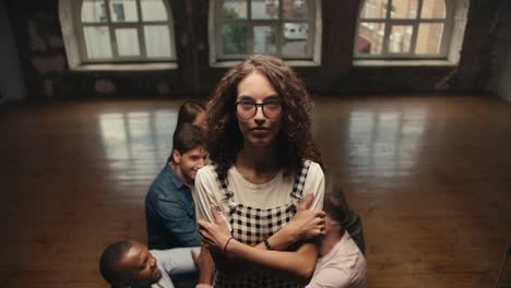 A-brunette-girl-with-curly-hair-wearing-glasses-in-a-checkered-jumpsuit-falls-into-the-arms-of-her-friends-in-group-therapy.-Practice-trust-between-people-in-a-group