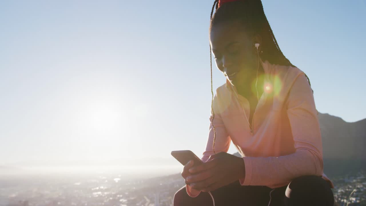 해가 지는 시골에서 스마트폰을 사용하여 야외에서 운동하는 행복한 아프리카계 미국인 여성