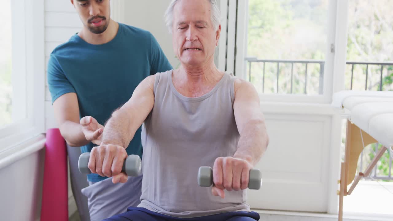 피트니스 스튜디오에서 두 인종의 남성 코치에 의해 덤벨로 운동하는 은퇴한 노인