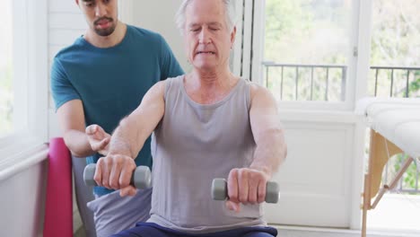 hombre jubilado haciendo ejercicio con pesas por un entrenador masculino biracial en un gimnasio