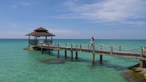 hermosa chica con un vestido blanco caminando en un muelle en el océano en una isla tropical