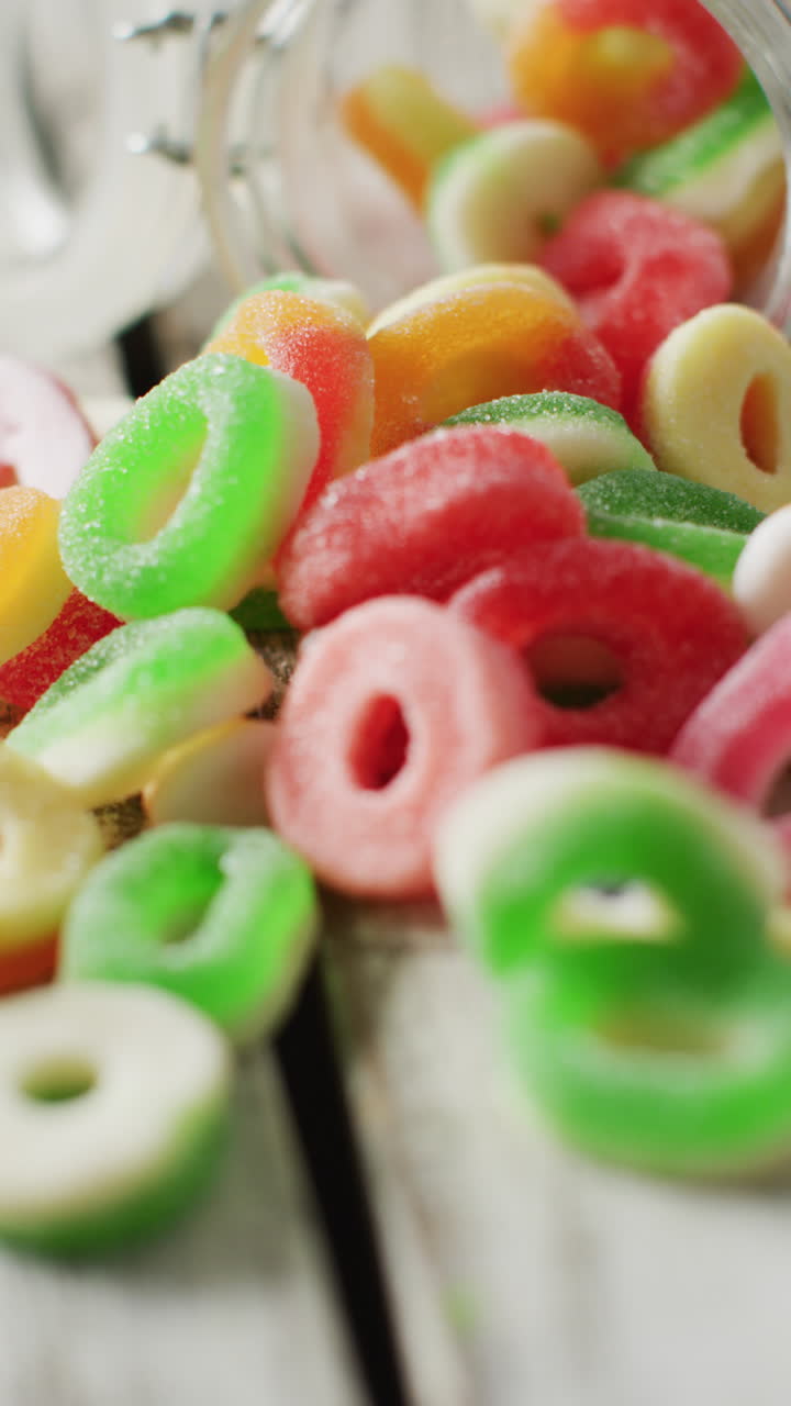 video vertical de caramelos de jalea derramándose de un frasco de vidrio sobre un fondo de madera