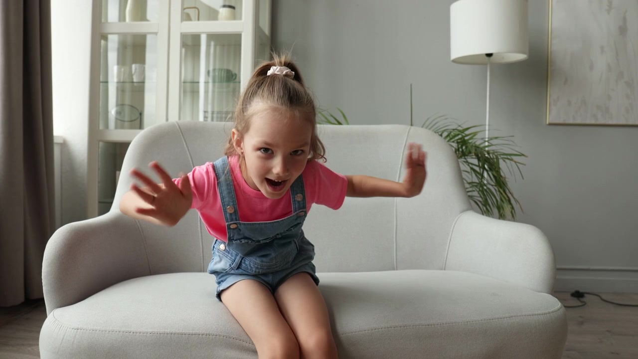 Cheerful Little Girl Sitting on Sofa Talking and Gesturing