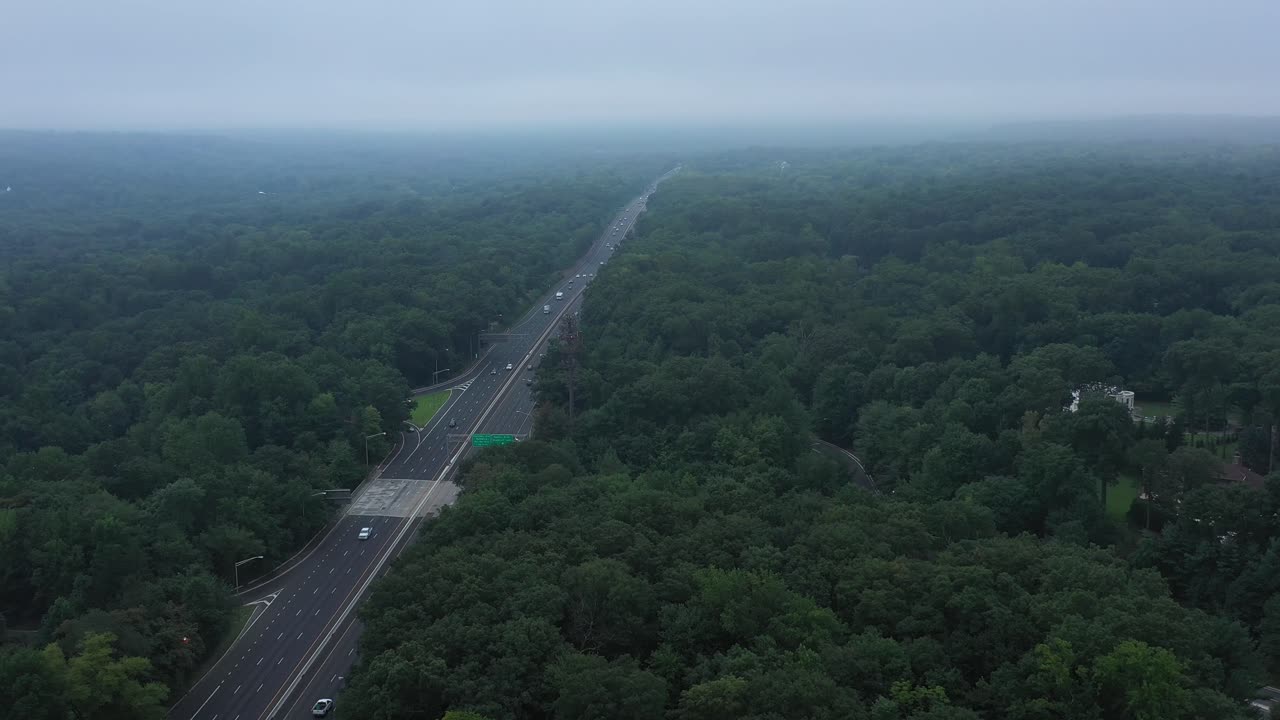 공중 영상은 아침 안개 속으로 교외 고속도로를 따라 나무 위로 이동합니다.